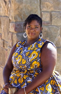 a woman in an african print dress leaning against a stone wall